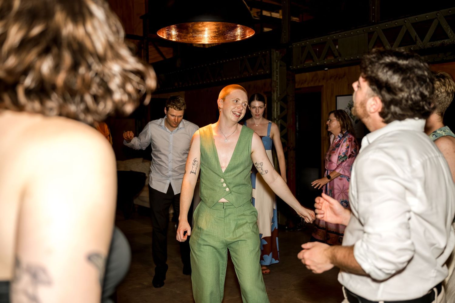 Joyful wedding guest in green jumpsuit dancing with friends at lively reception party.