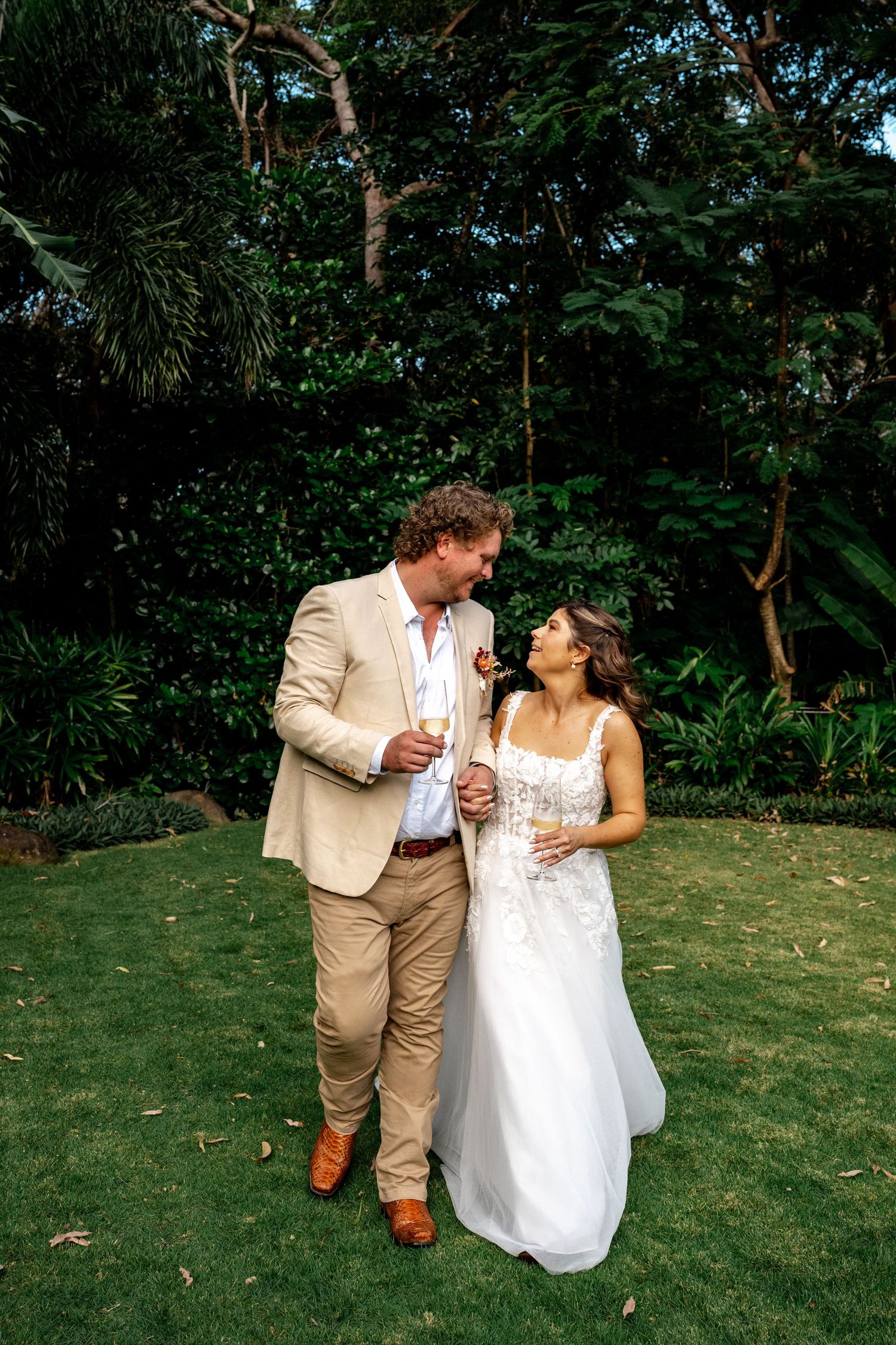 Bride and groom sharing a romantic moment on lush green lawn surrounded by tropical gardens.