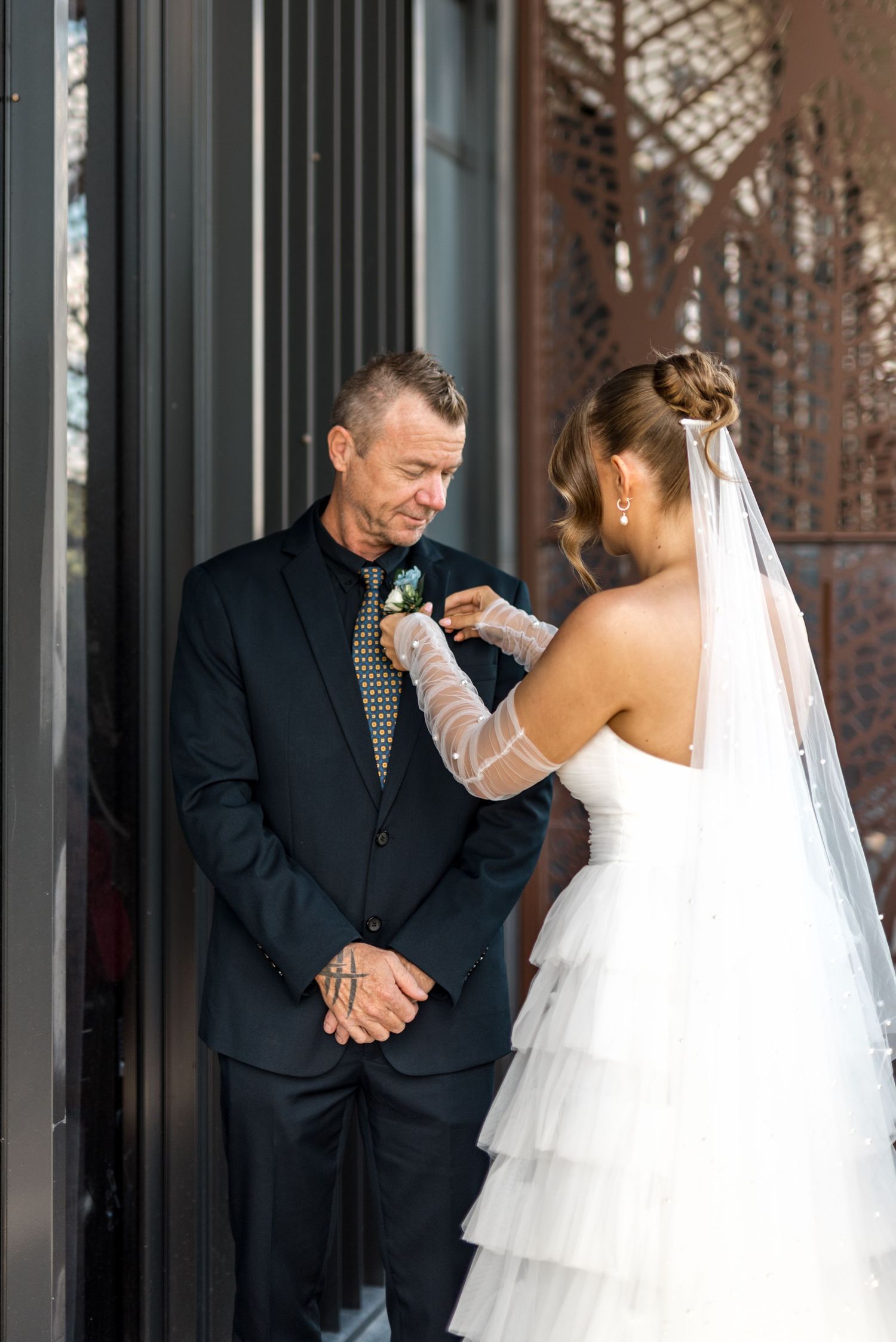Bride in white ruffled gown pinning boutonniere on groom in black suit at wedding.