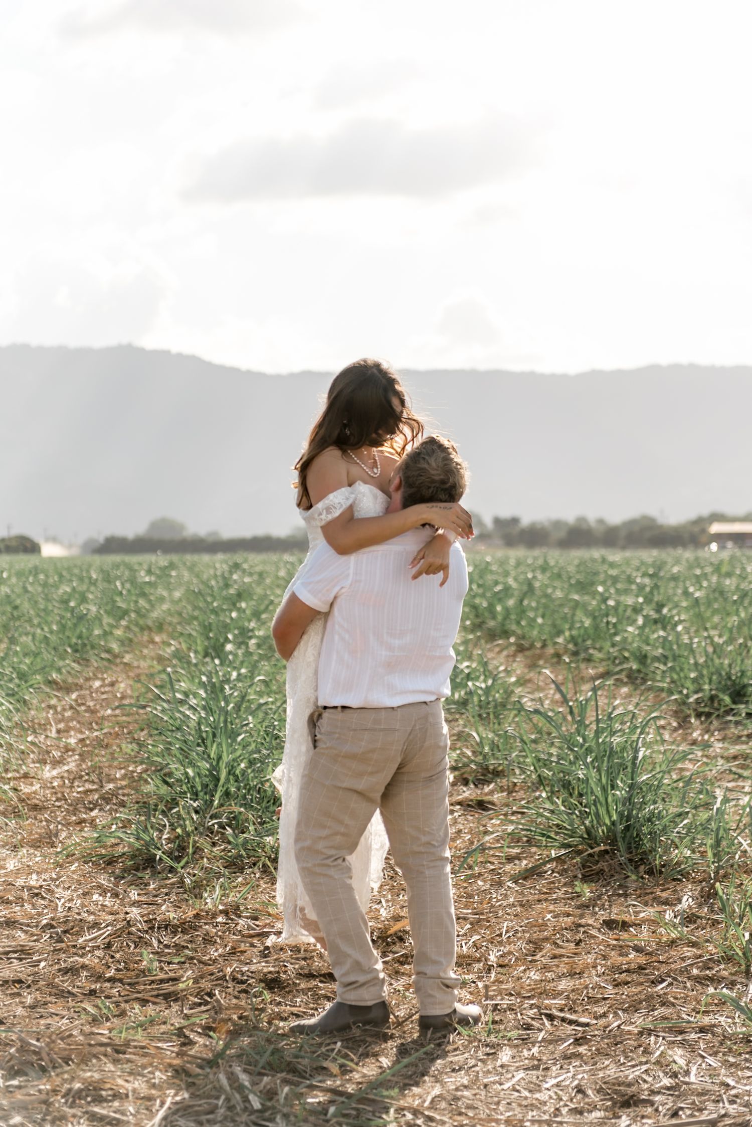 Groom sweeping bride off her feet in a joyful embrace in a scenic green countryside field.