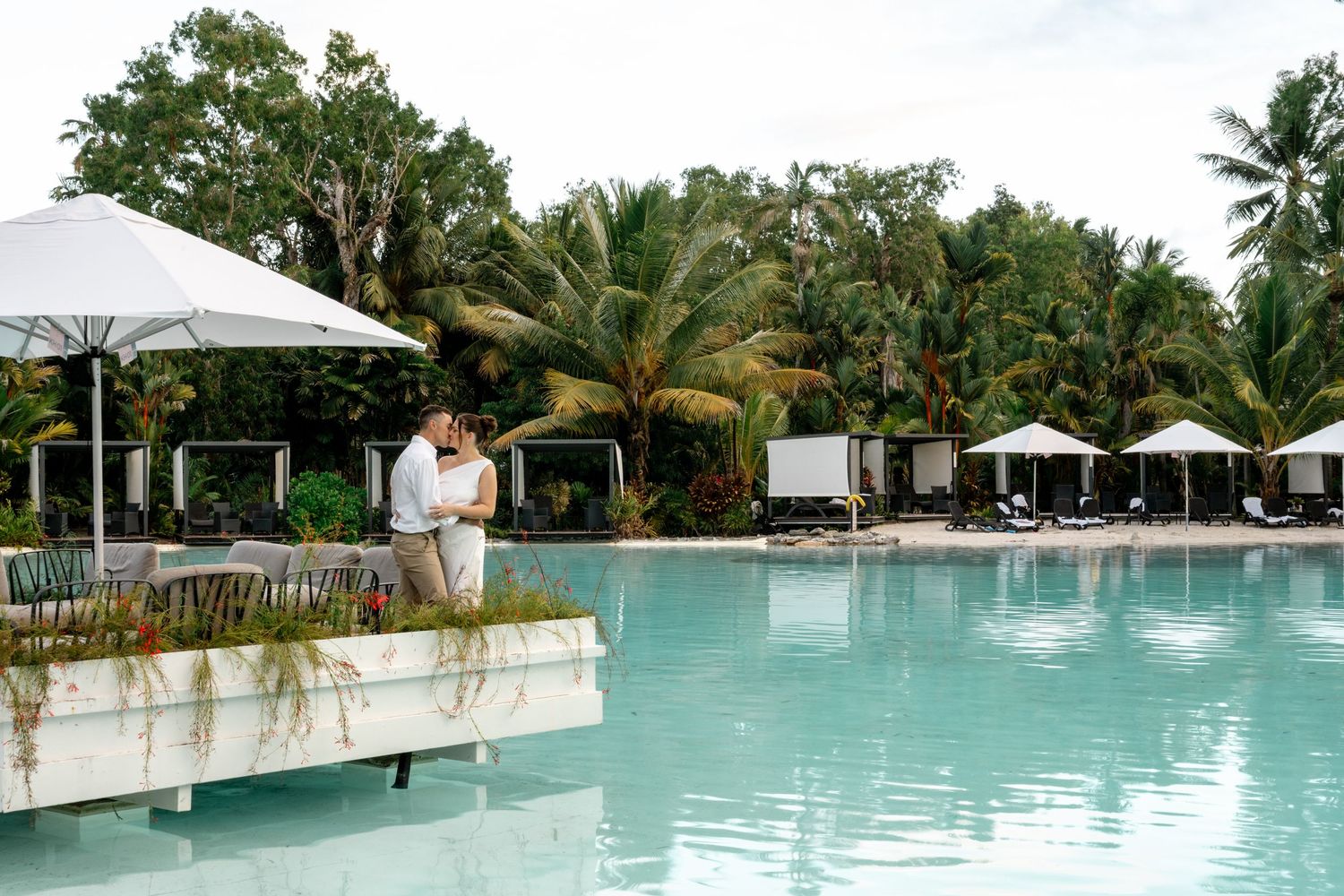 Romantic couple sharing a kiss on a pool deck at a tropical resort with palm trees at Sheraton Grand Mirage Port Douglas.