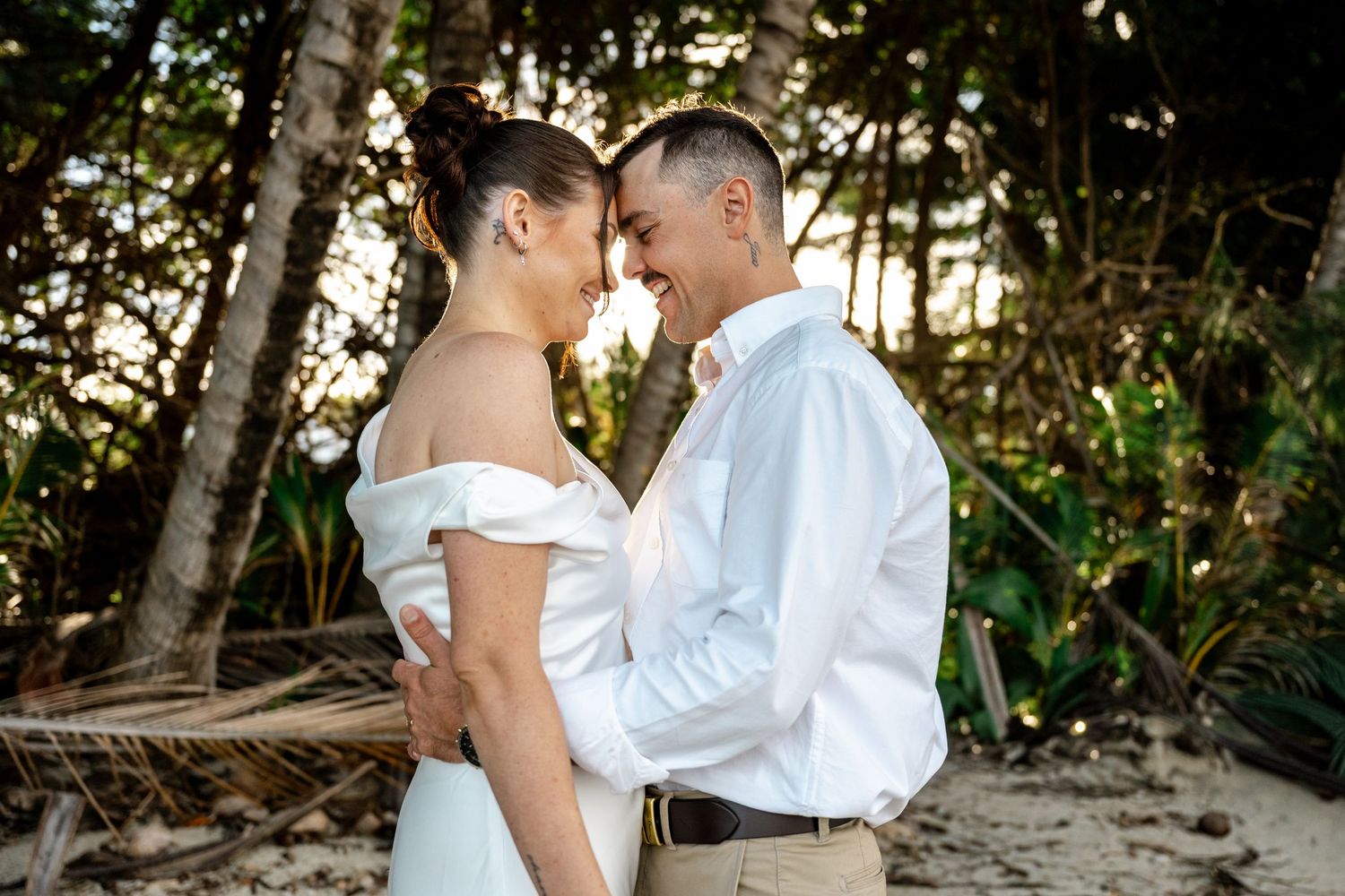 Laughing newlyweds share a romantic moment face-to-face on a sunlit tropical beach wedding day at Four Mile Beach, Port Douglas.