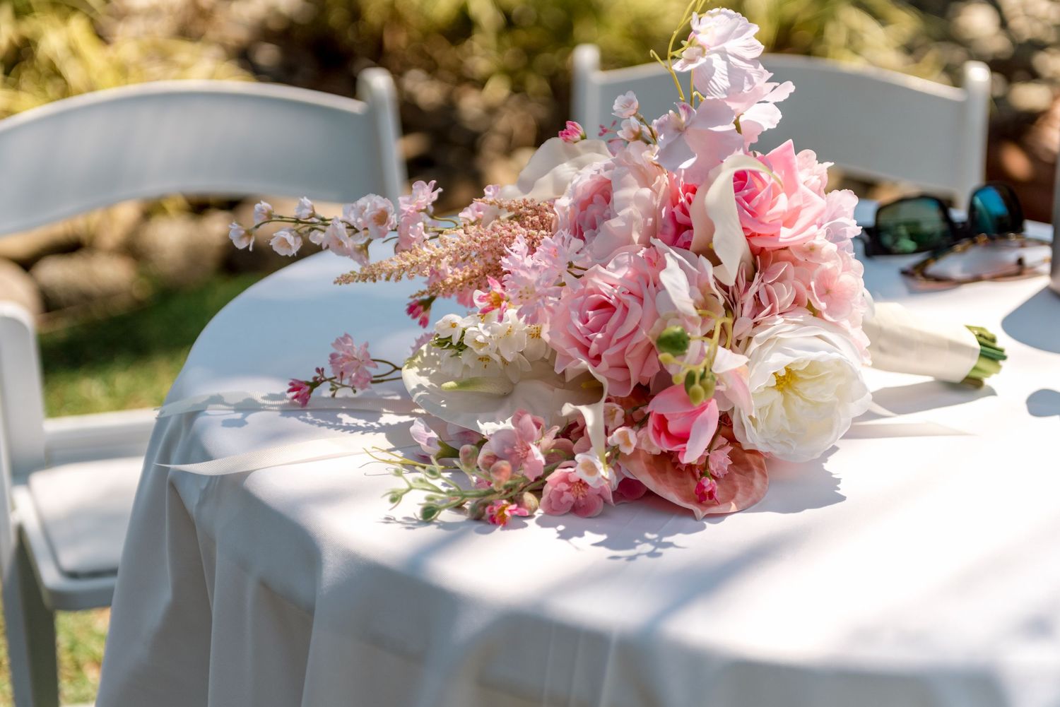 Pink bridal bouquet with roses and delicate blooms resting on white linen covered table outdoors.