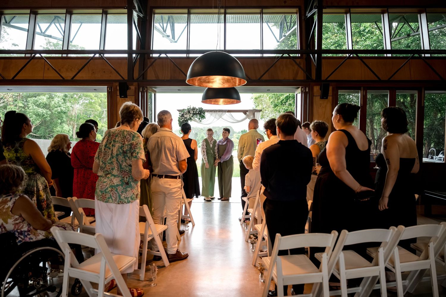 Wedding guests stand and gather around a couple during an intimate barn ceremony outdoors.