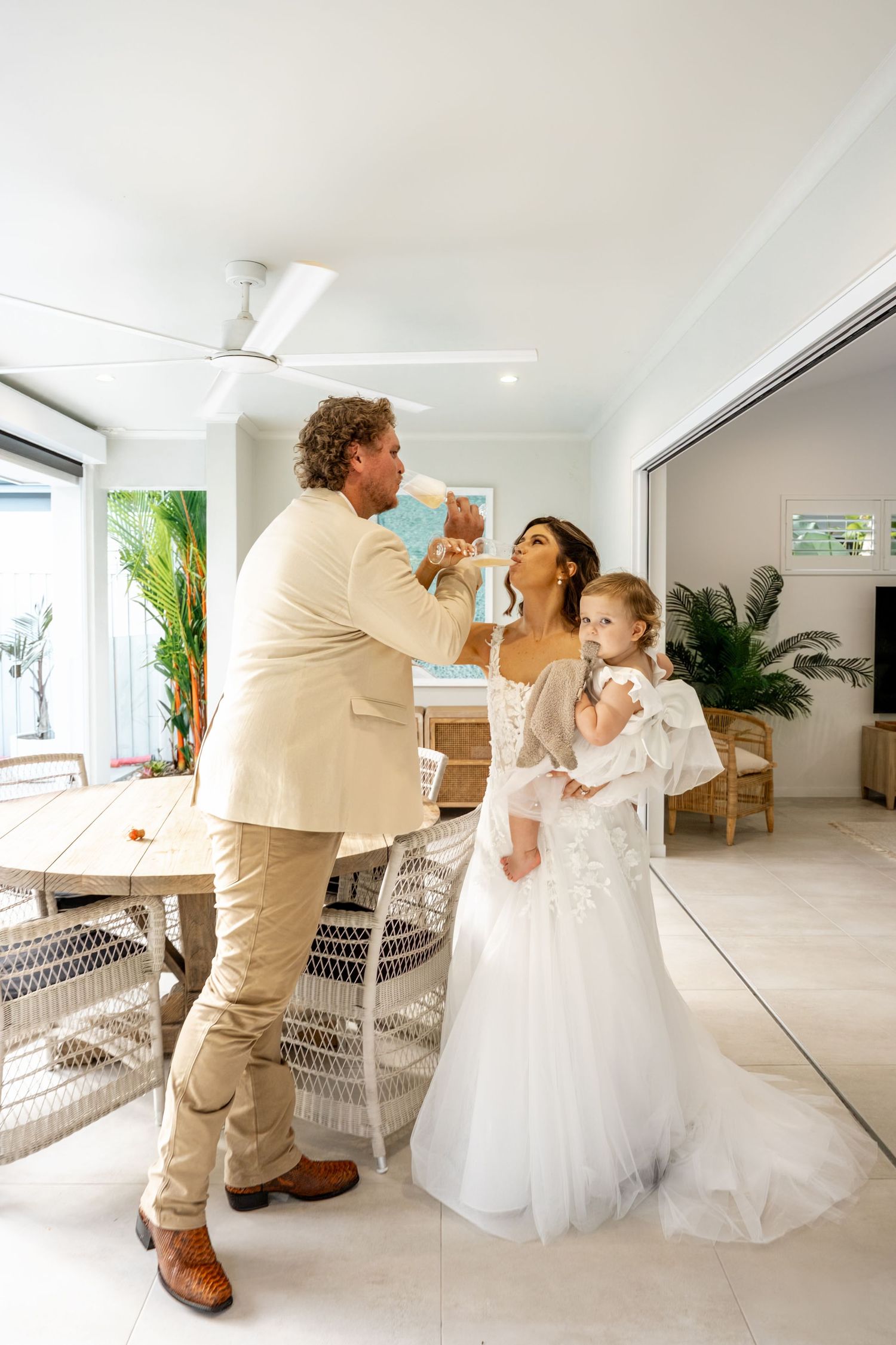 Bride and groom toasting champagne indoors with young girl in white dress at intimate wedding celebration.