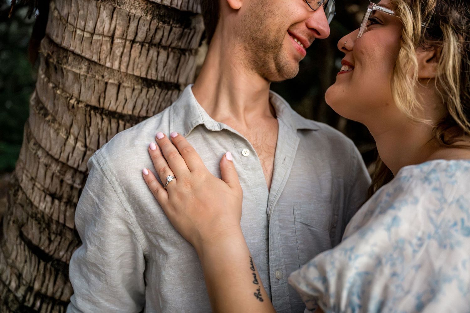 Close-up of smiling couple sharing a romantic moment leaning against a palm tree trunk at Four Mile Beach, Port Douglas.