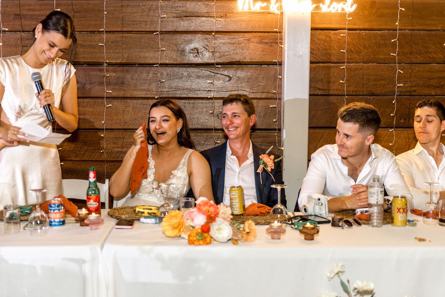 Bride and groom laughing during wedding speech at decorated head table.