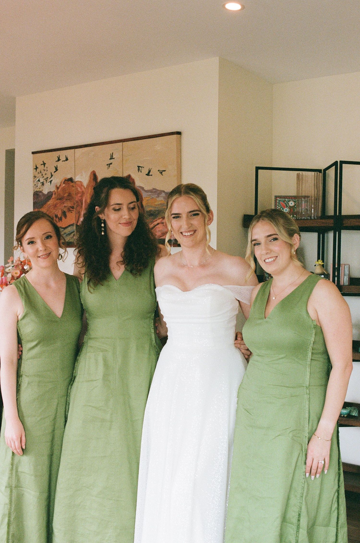 Bride in white dress posing with three bridesmaids wearing matching sage green gowns.