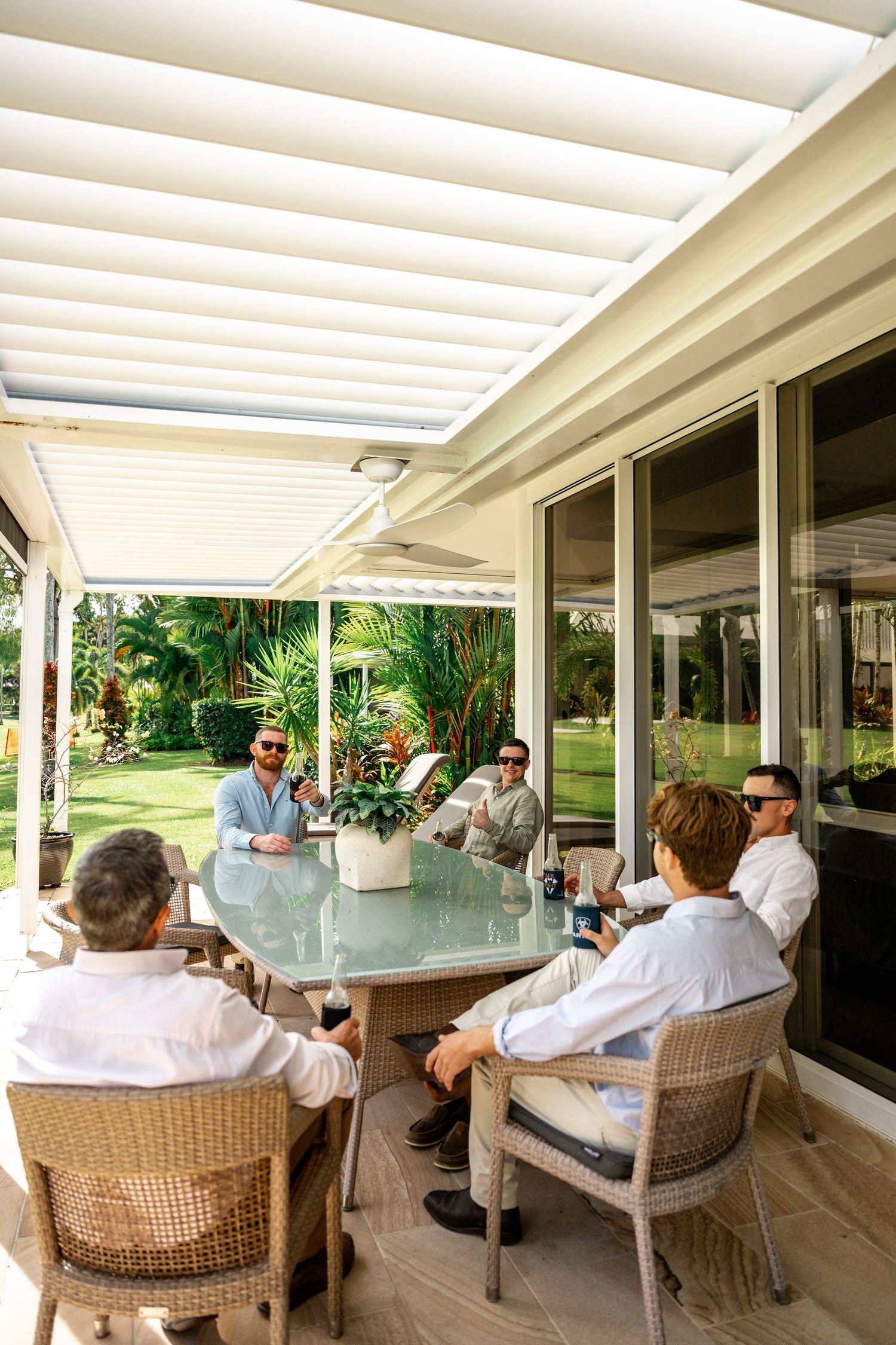 Groomsmen gathered around outdoor patio table under pergola in tropical garden setting before wedding.