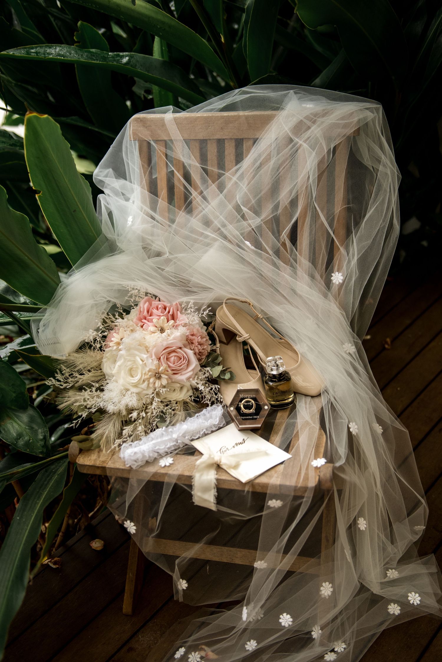 Bridal veil, bouquet, heels, and accessories styled on a wooden chair surrounded by tropical greenery.