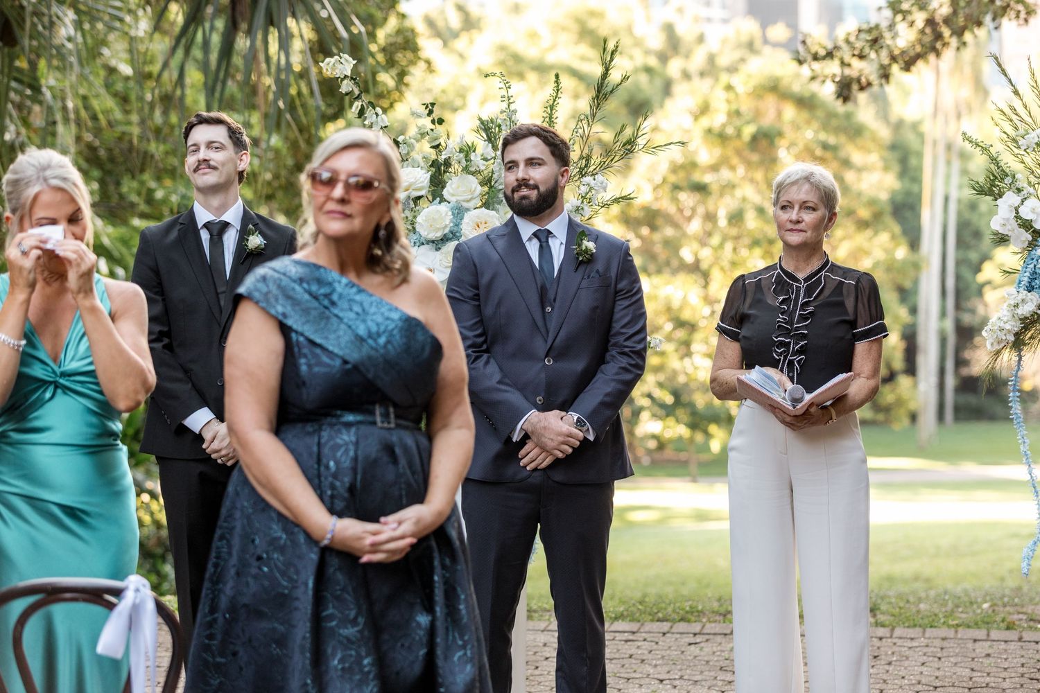 Wedding guests and groom await bride at elegant outdoor garden ceremony with floral arch.