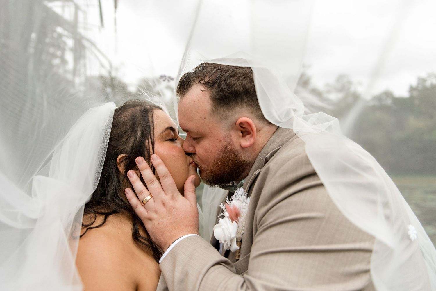 Bride and groom share a passionate kiss under a flowing white veil on their wedding day.