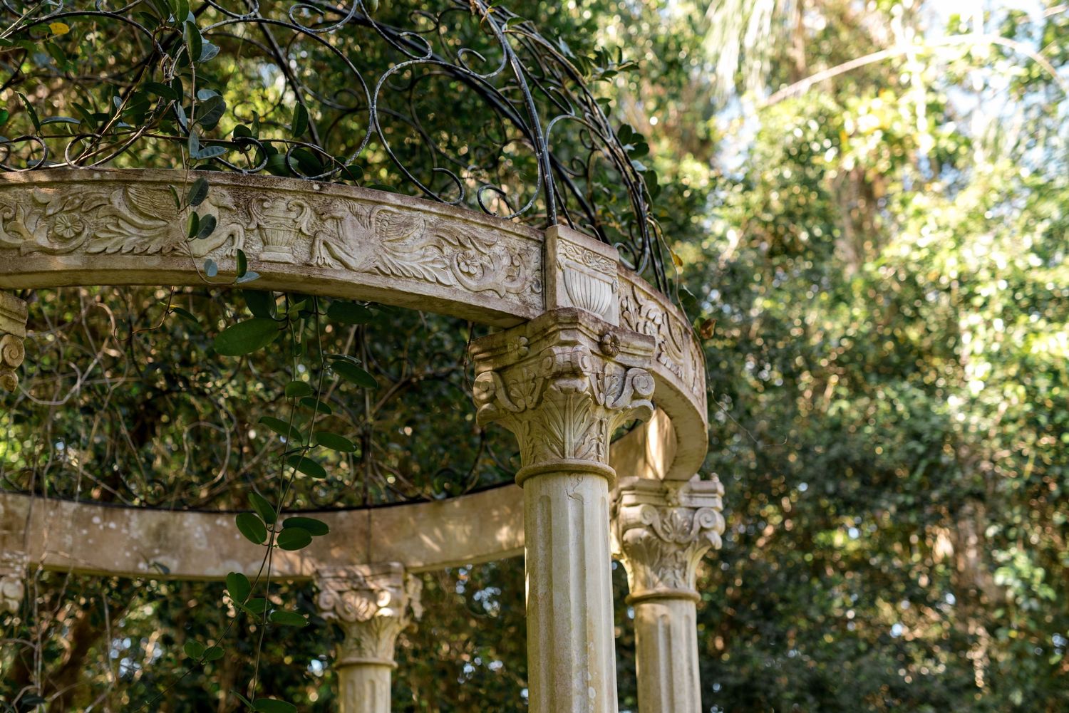 Close-up of an ornate stone wedding gazebo with carved details and climbing vines in a garden.