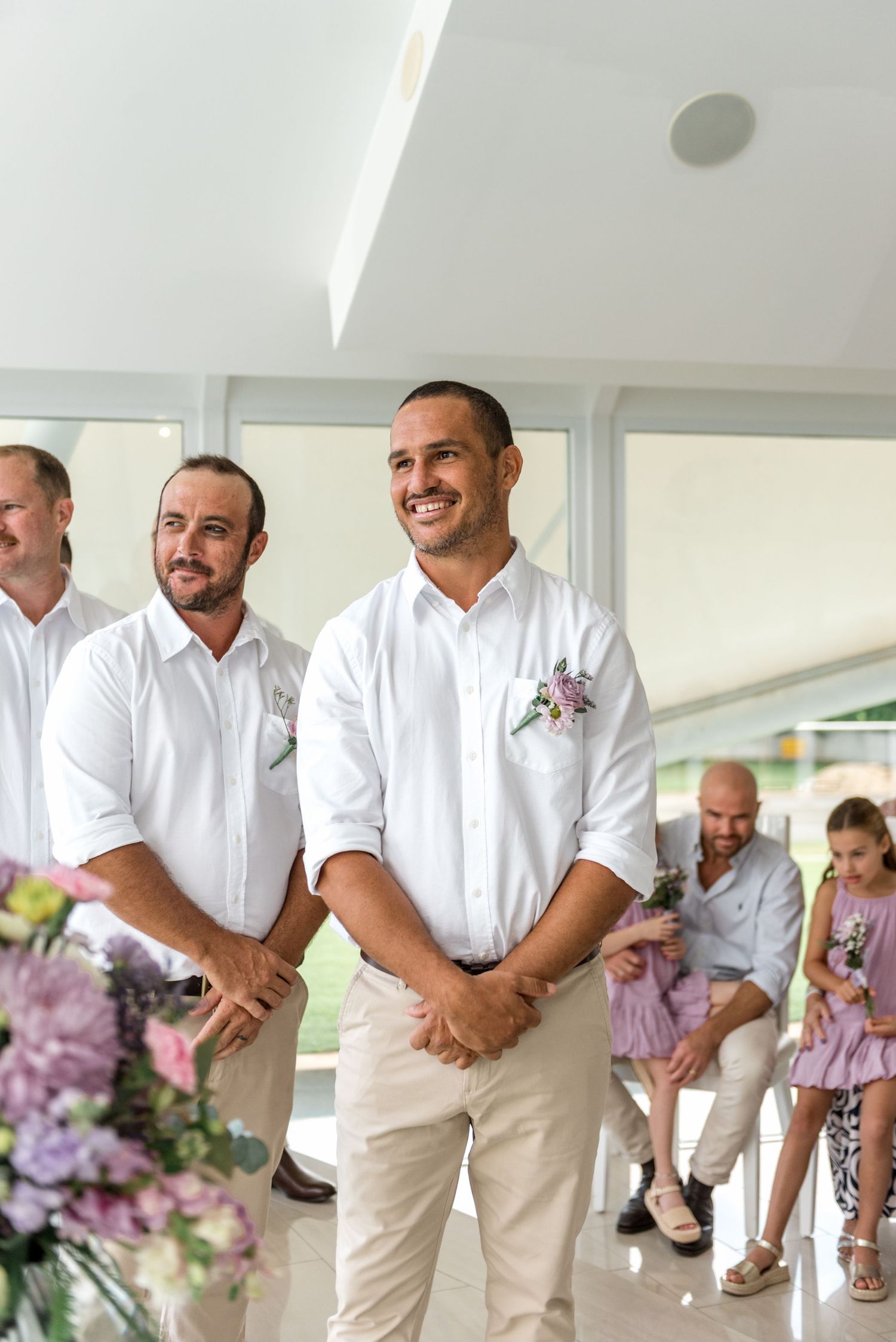 Smiling groom in white shirt with floral boutonniere awaiting bride at altar.