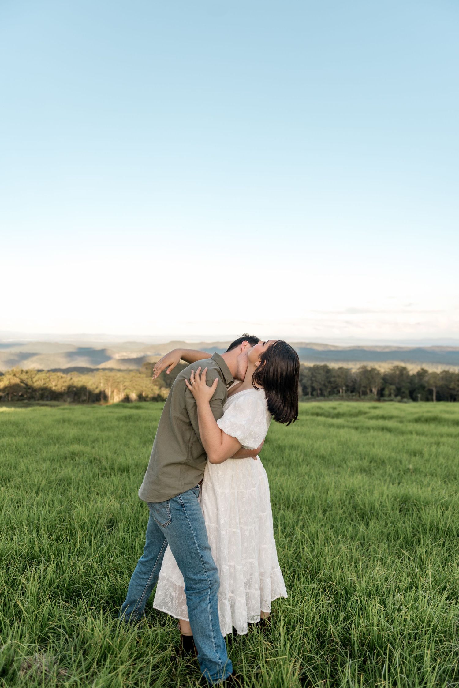 Romantic couple kissing with a dip in a lush green field at dusk.