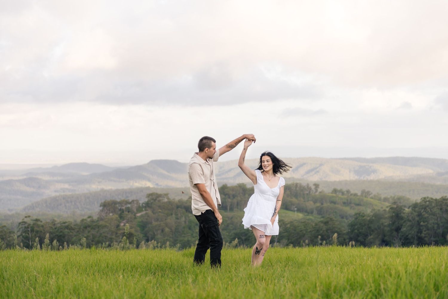 Couple twirling and dancing together in a vibrant green meadow with mountain views.