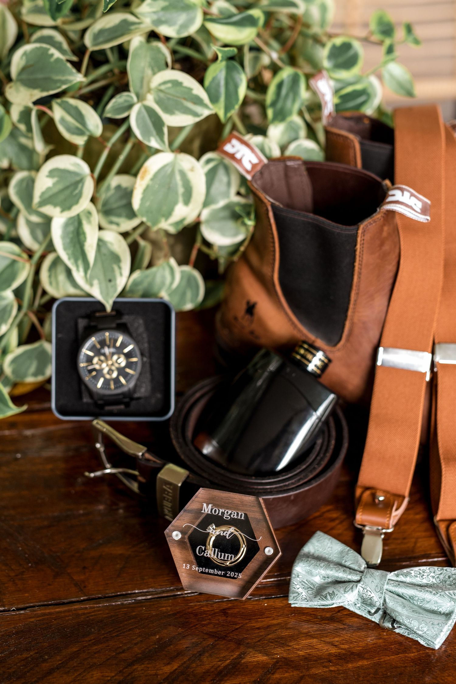 Groom's wedding accessories including leather boots, suspenders, flask, bow tie, and personalized ring box.