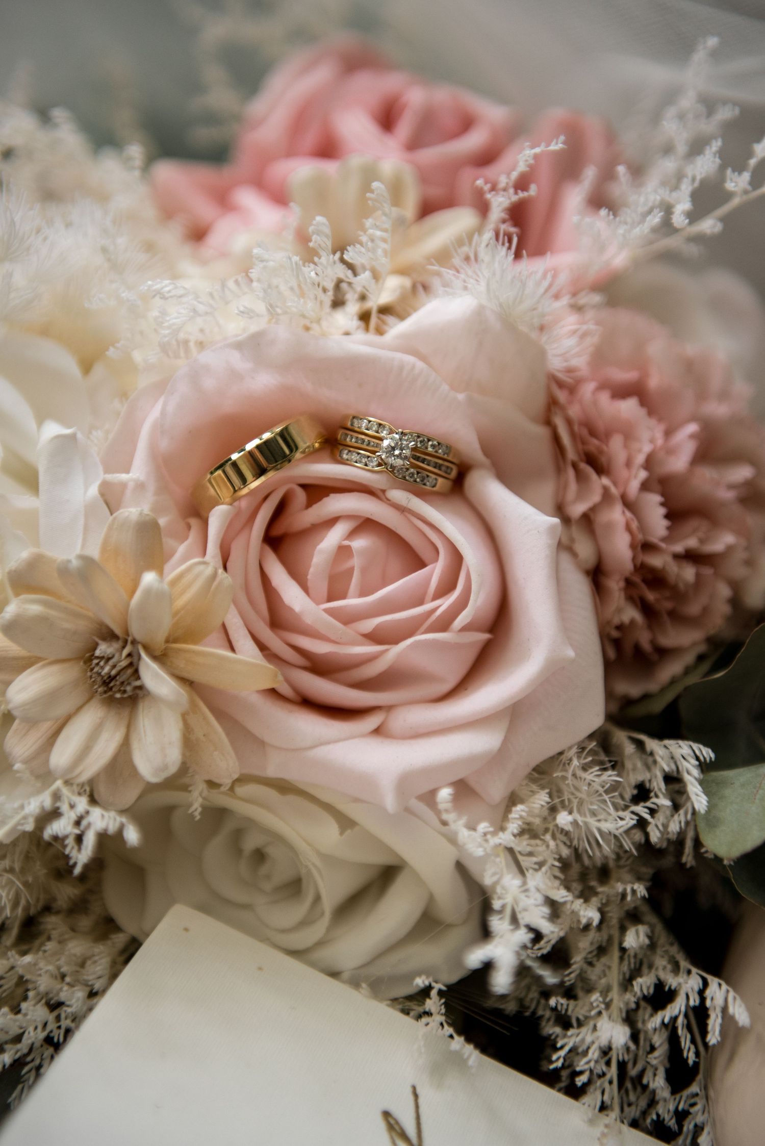 Two gold wedding bands resting on a blush pink rose in a romantic bridal bouquet.