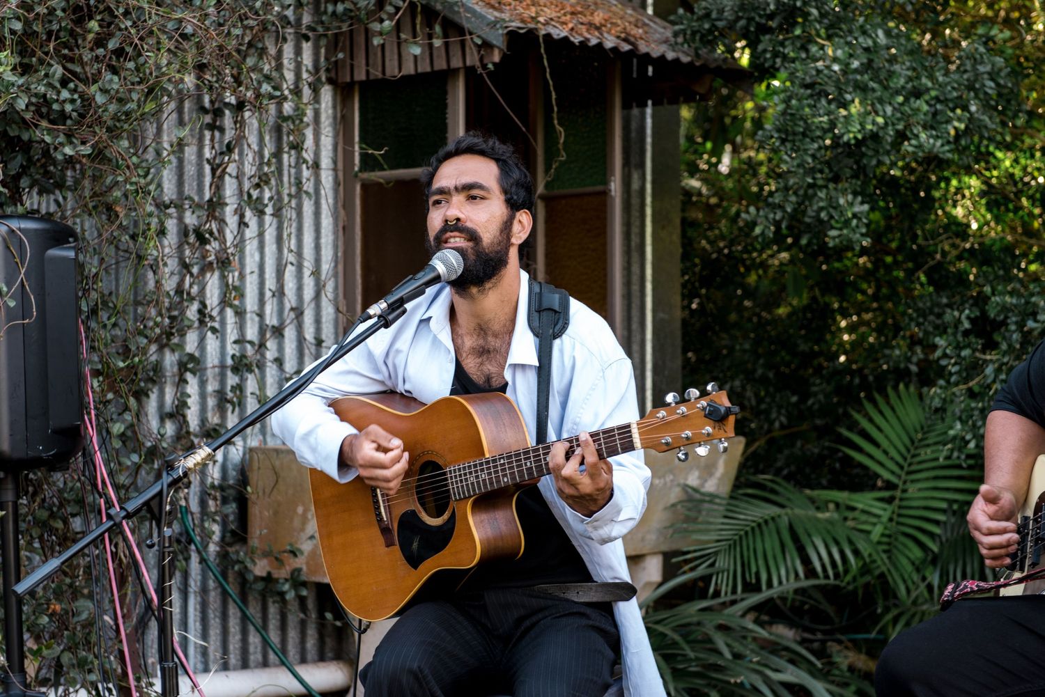 Male musician plays acoustic guitar and sings into microphone at outdoor wedding reception.