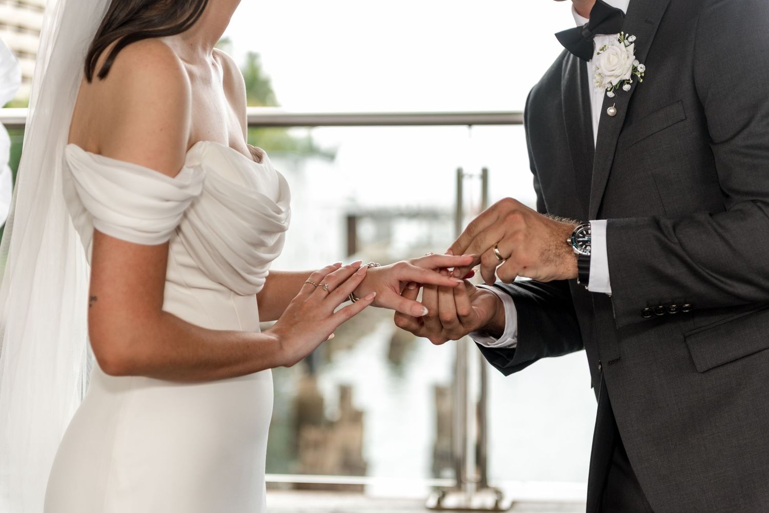 Close-up of groom sliding wedding ring onto brides finger during waterfront ceremony.