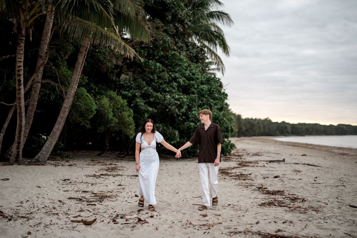 Happy couple walking hand in hand along a sandy tropical beach lined with palm trees.