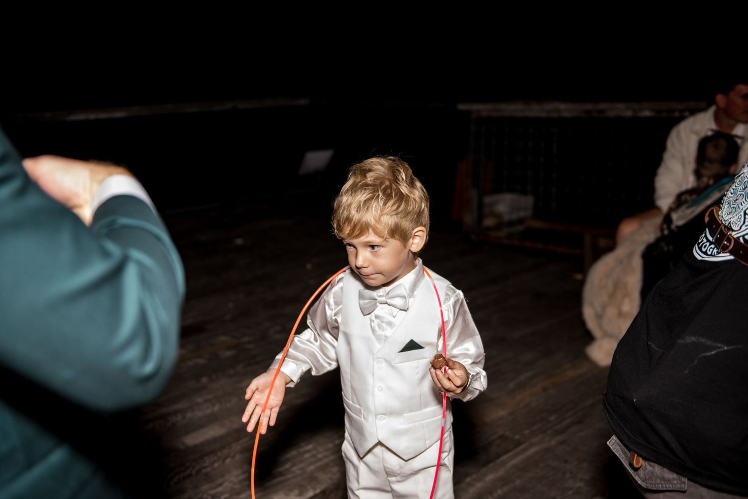 Young boy in white suit holds a hula hoop on the dance floor at a wedding reception.