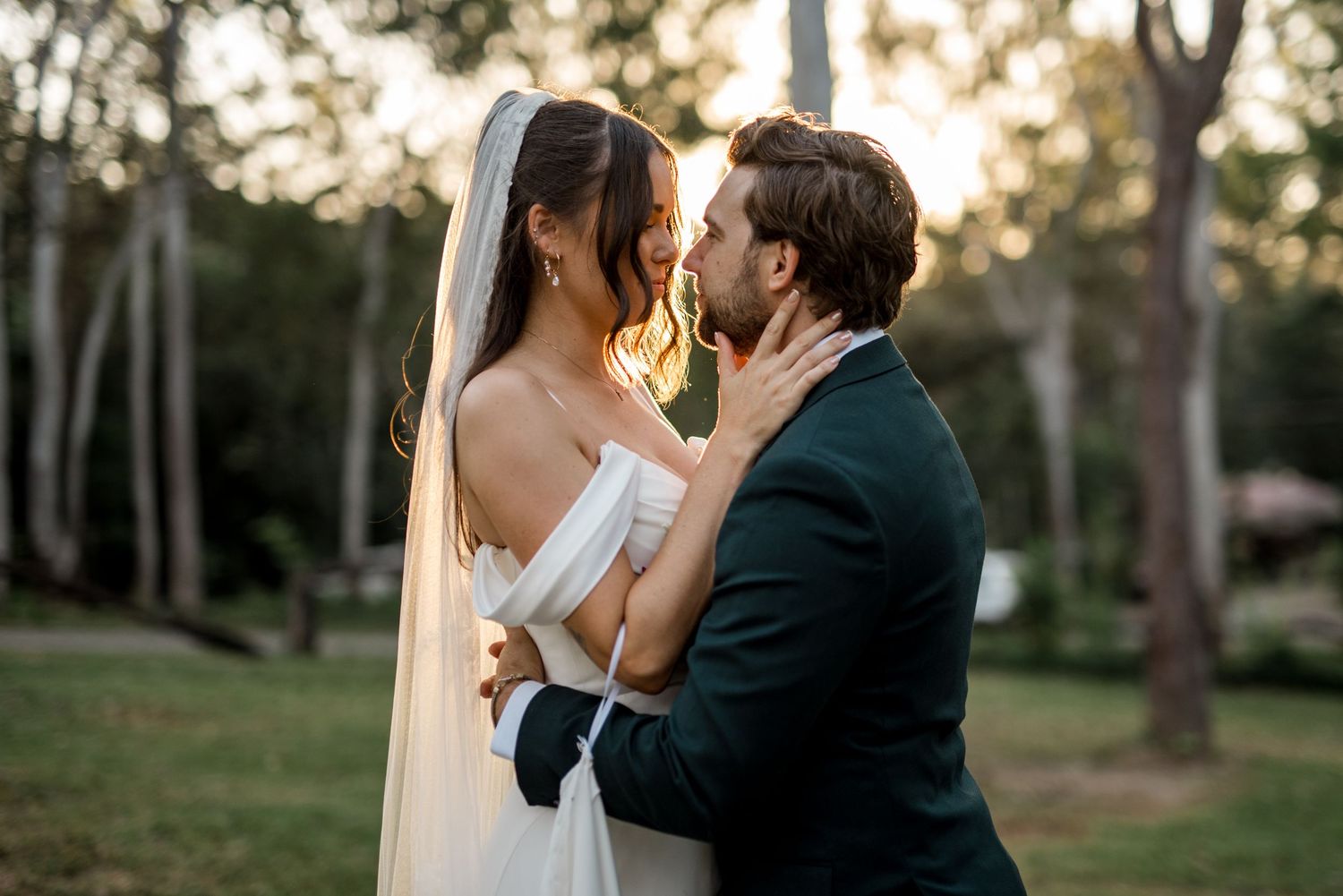 Bride and groom sharing a romantic almost-kiss in a sunlit garden on their wedding day.
