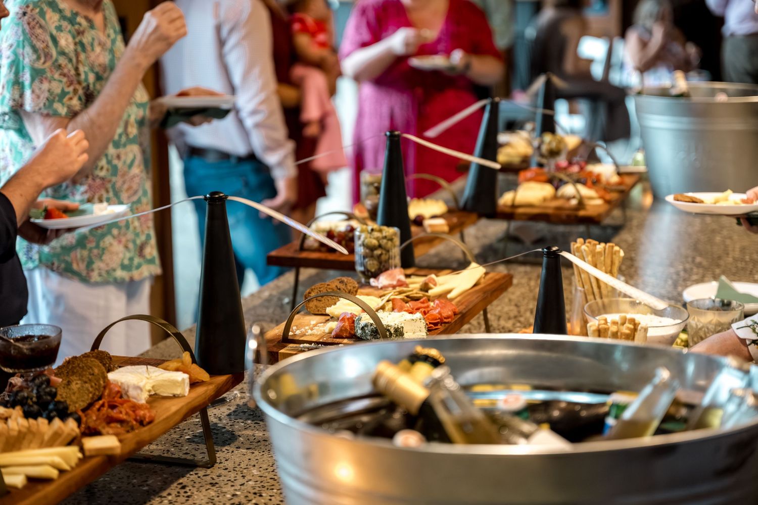 Guests browse elaborate wedding grazing table with charcuterie boards and assorted snacks.