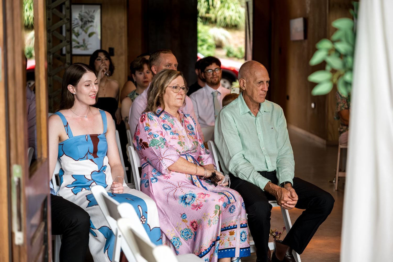 Smiling wedding guests seated in white chairs at a rustic timber wedding venue.