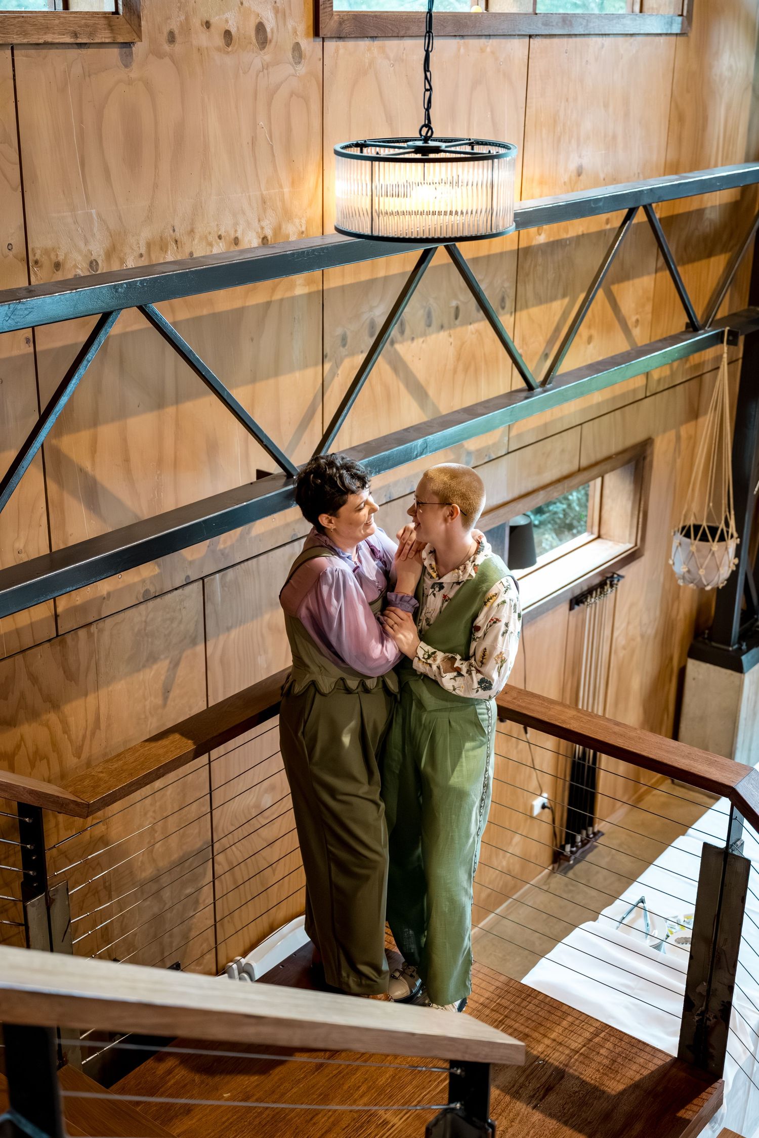 Two women share a romantic moment on a wooden staircase landing in a rustic interior.