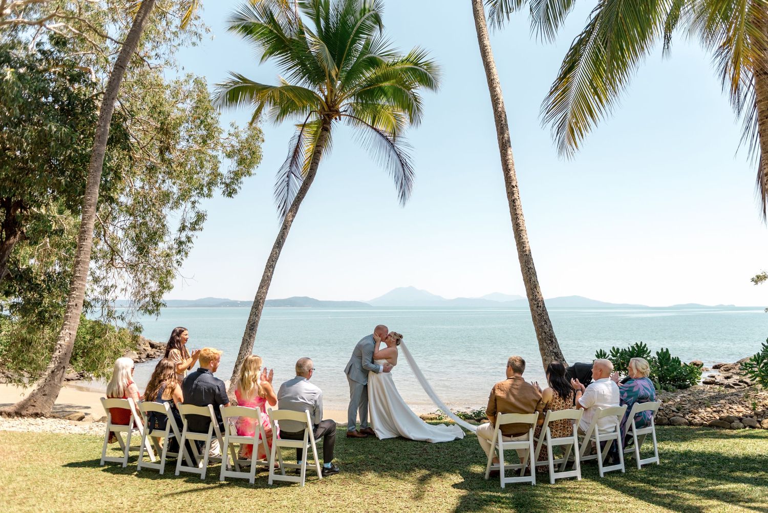Intimate beach wedding ceremony under palm trees with ocean backdrop.