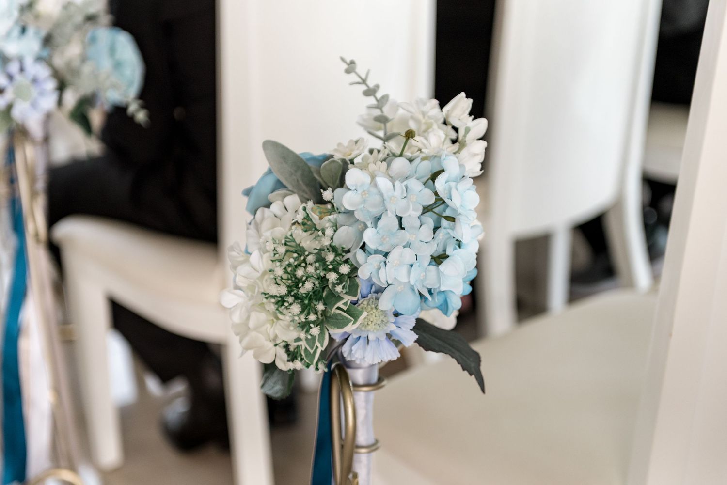 Elegant blue and white hydrangea floral arrangement decorating wedding ceremony chair aisle.