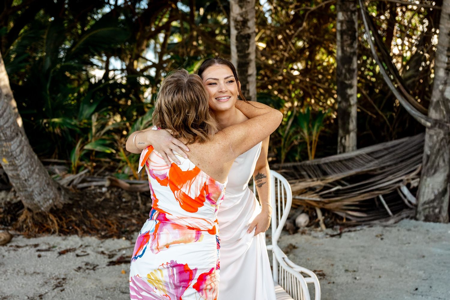 Smiling bride in white dress hugging a guest in a colorful outfit on a tropical beach at Four Mile Beach, Port Douglas.