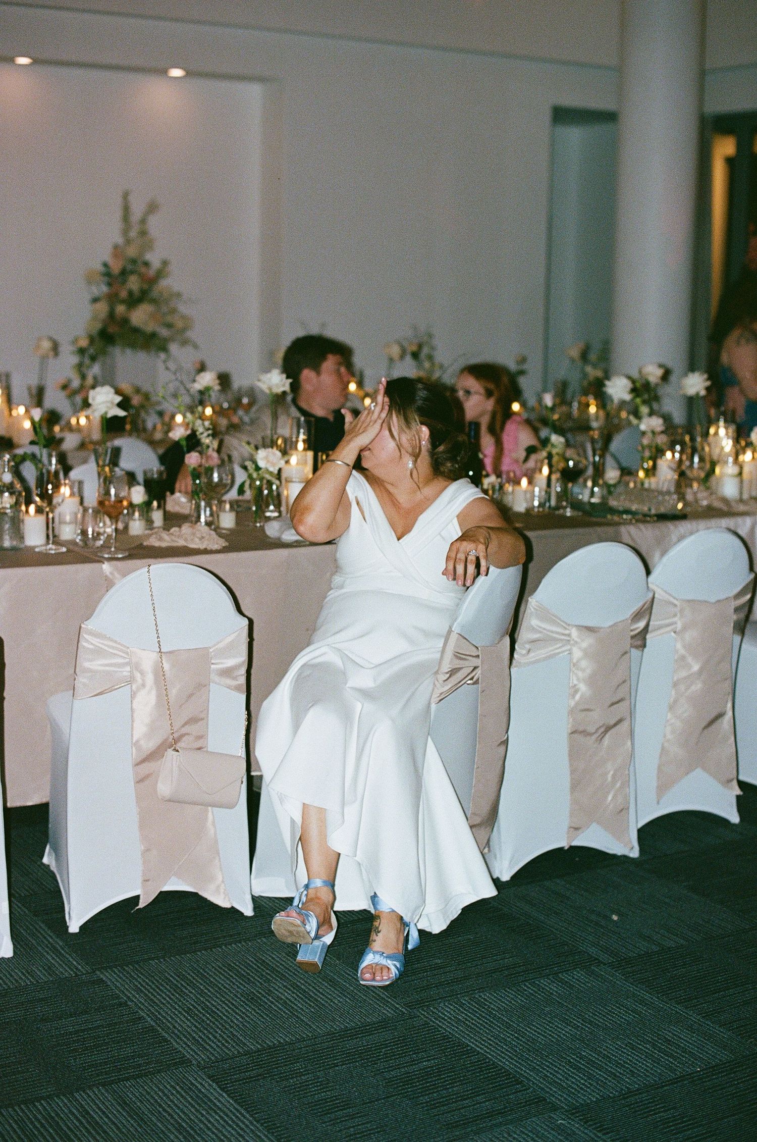 Bride in white wedding dress laughing while seated at decorated wedding reception.