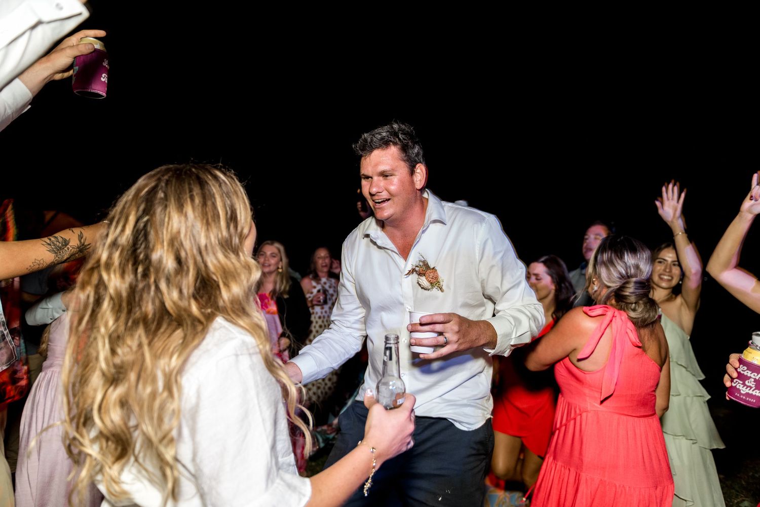 Man in white shirt dancing with guests at a lively outdoor night wedding reception.