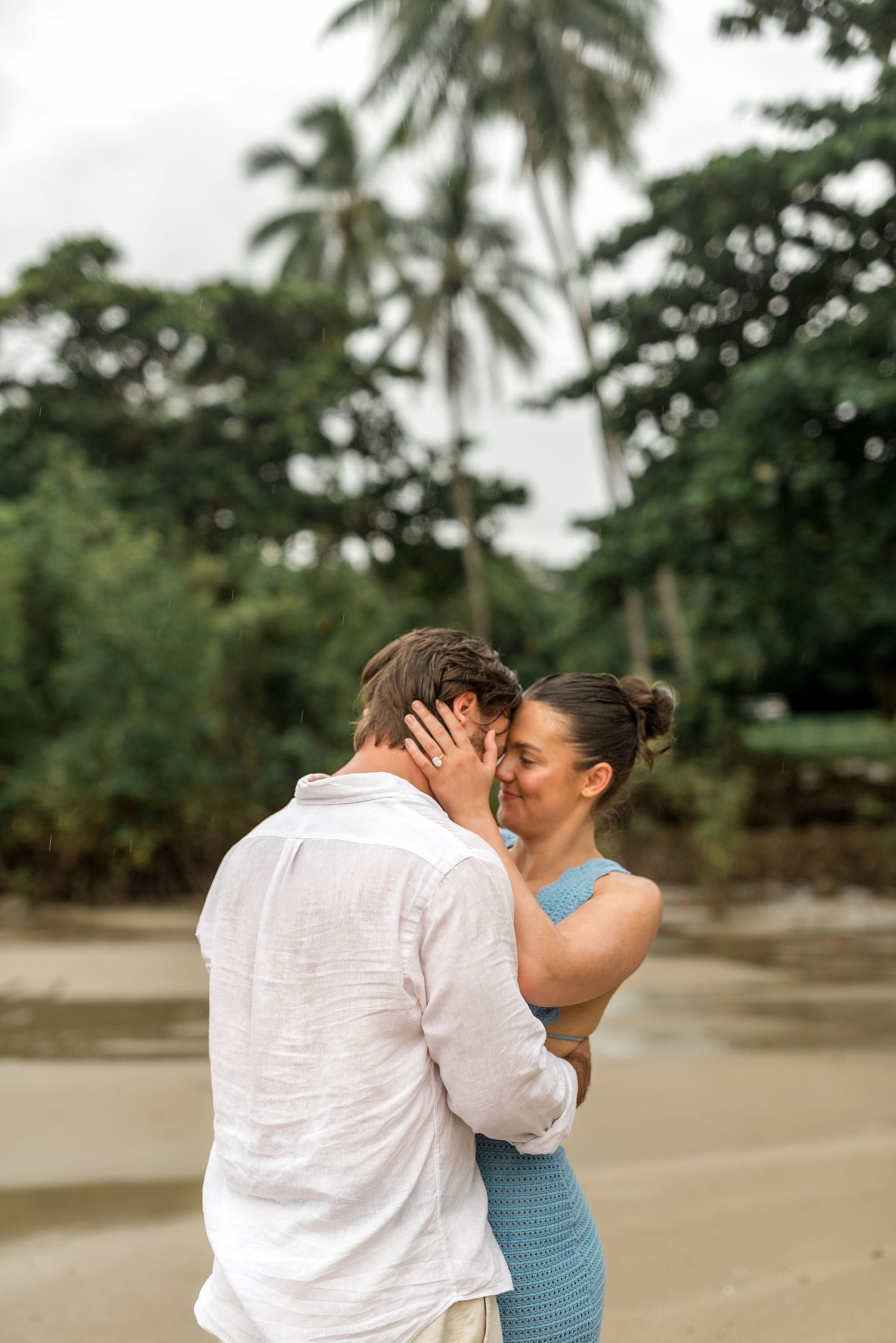 Couple sharing an intimate moment on a tropical beach surrounded by palm trees and lush greenery.