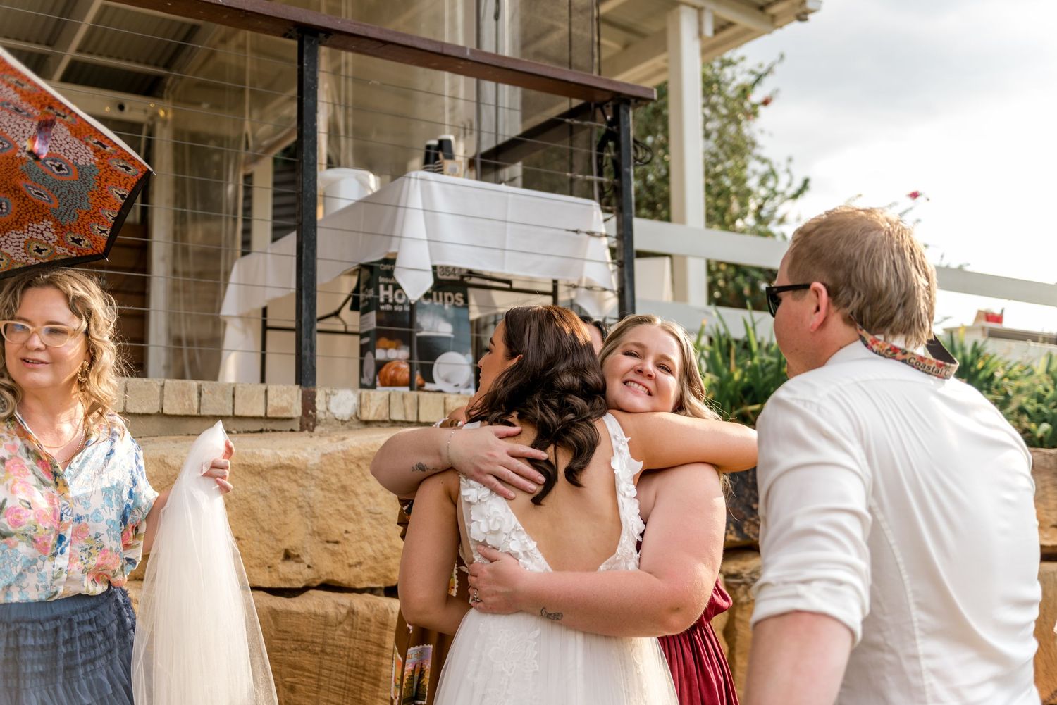 Bride sharing a warm hug with a guest at an outdoor wedding reception venue.