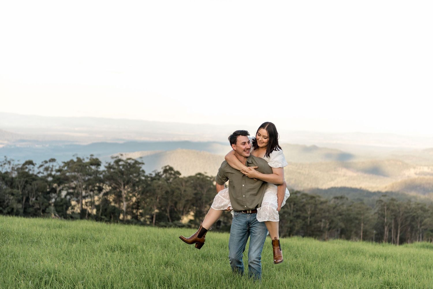 Man joyfully lifting woman in his arms in a scenic green hillside meadow.