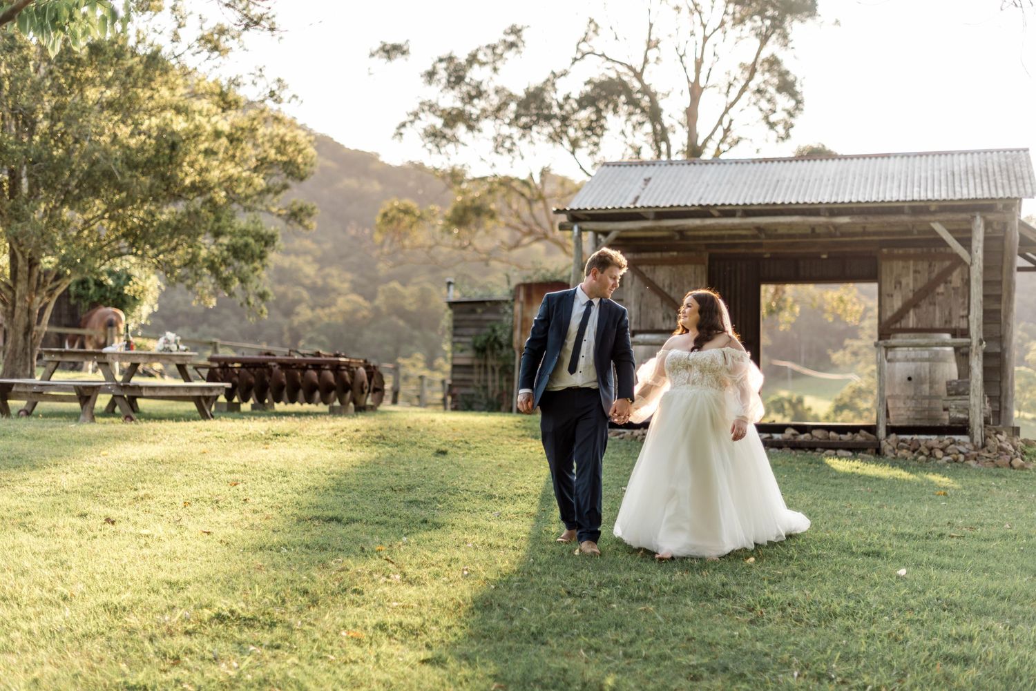 Bride and groom walk hand in hand across green lawns at a picturesque farm wedding venue.