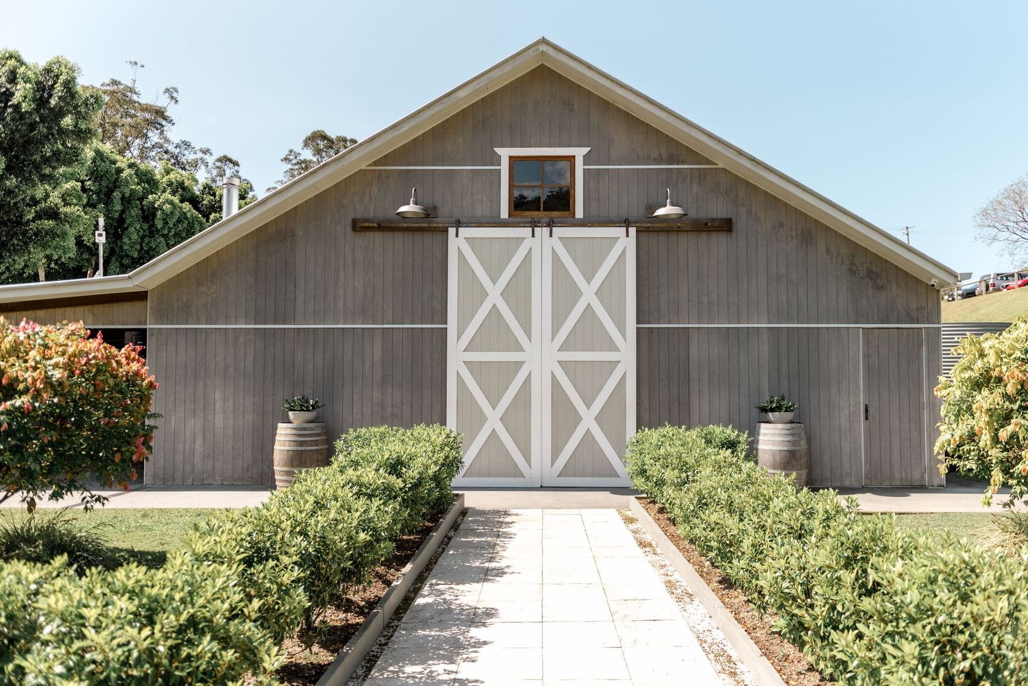 Rustic gray barn wedding venue with white cross doors and manicured garden pathway.