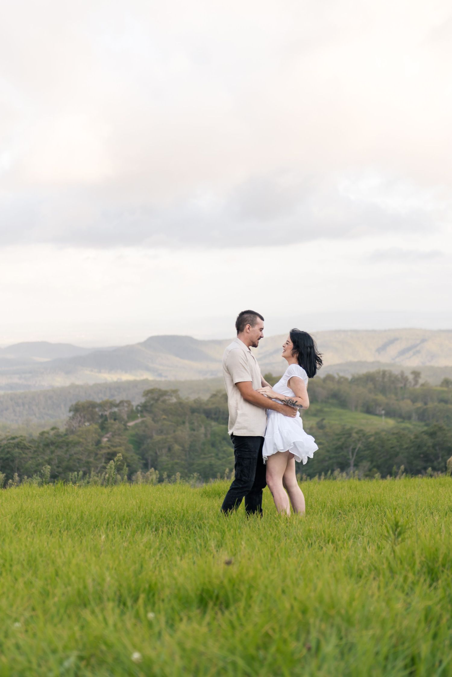 Happy couple laughing and holding each other in a green meadow with hills behind.