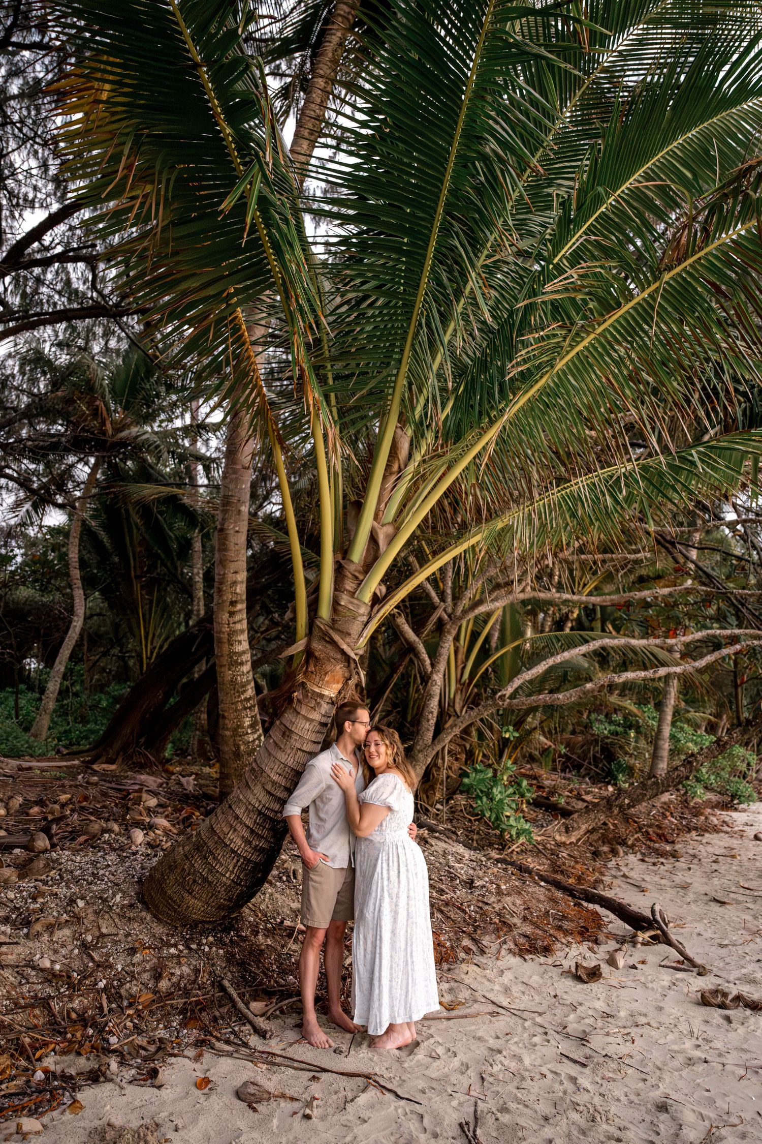 Loving couple embracing under a large palm tree on a sandy tropical beach shoreline at Four Mile Beach, Port Douglas.