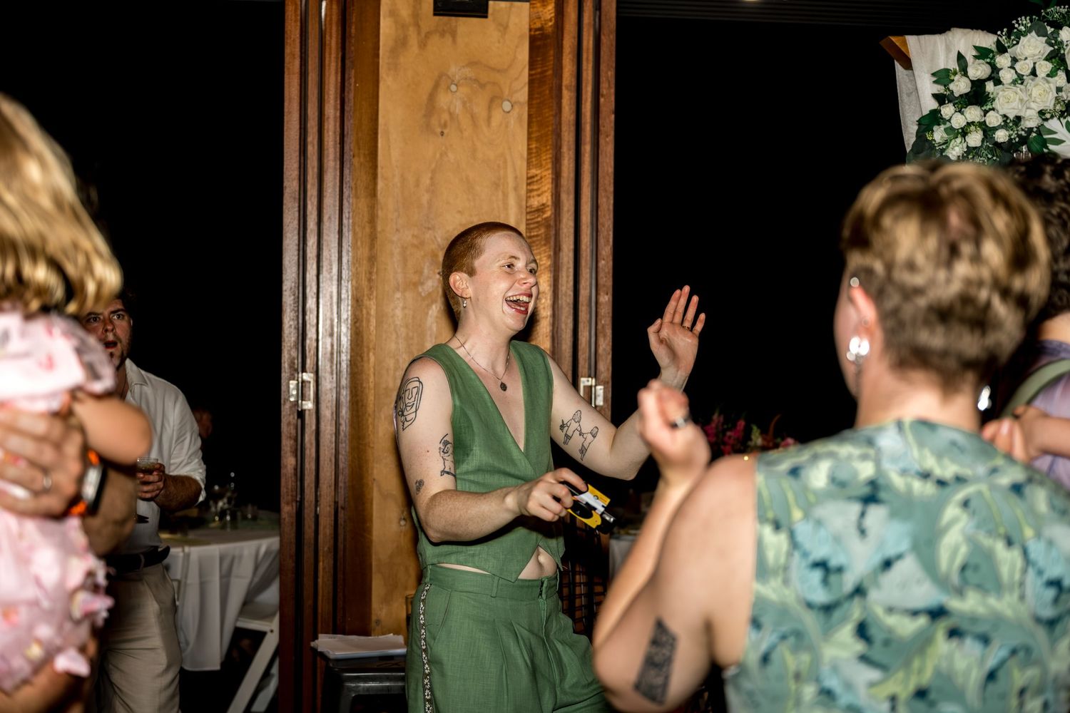 Joyful wedding guest in green dress laughs and claps at a lively reception.