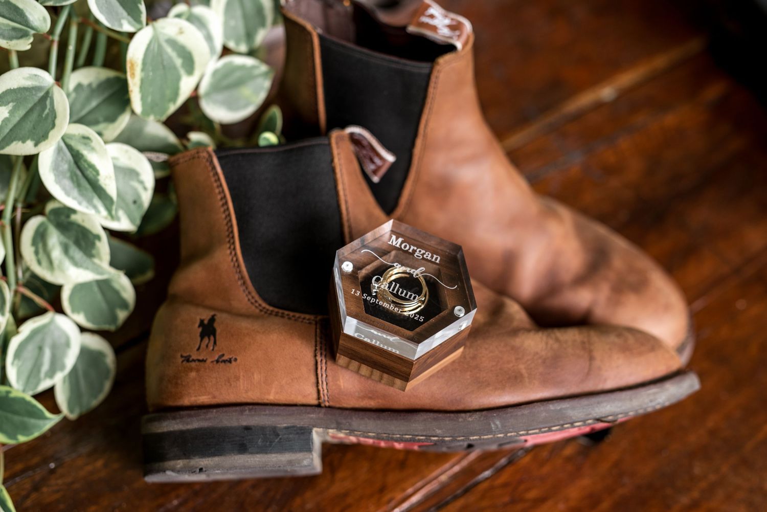 Brown leather Chelsea boots with a hexagonal wedding ring box on a wooden surface.