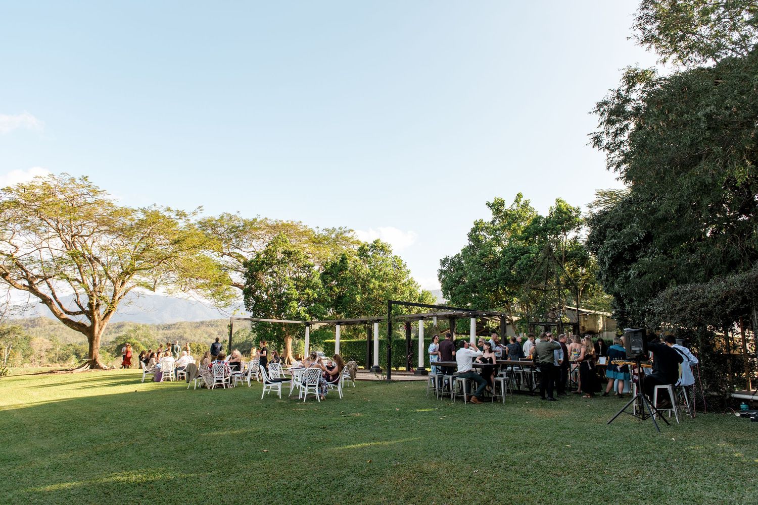 Wedding guests gather on green lawn at elegant outdoor reception venue at dusk.
