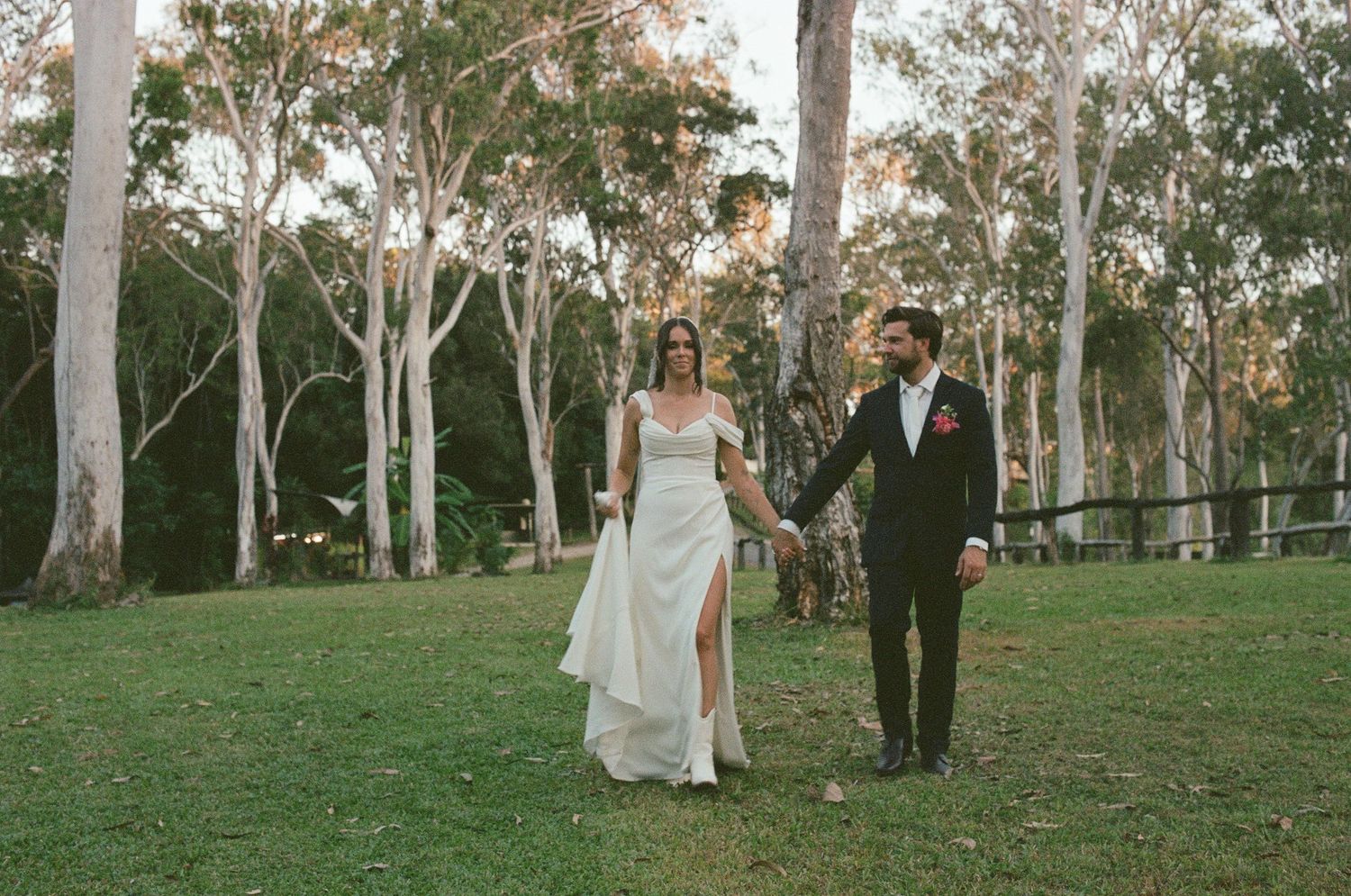 Bride and groom holding hands walking through eucalyptus tree garden at wedding.