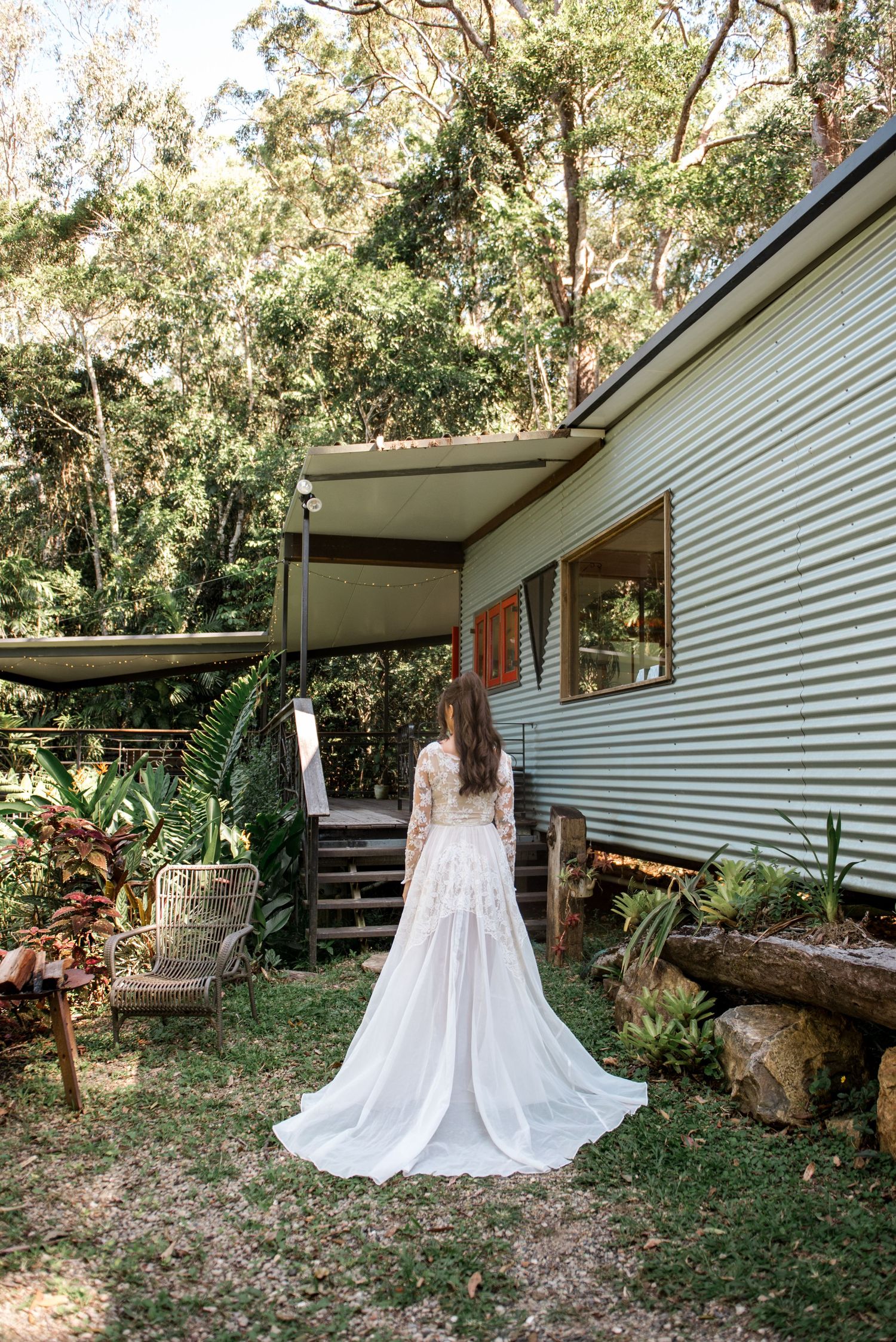 Bride in flowing white lace wedding dress standing outside a rustic forest cabin.
