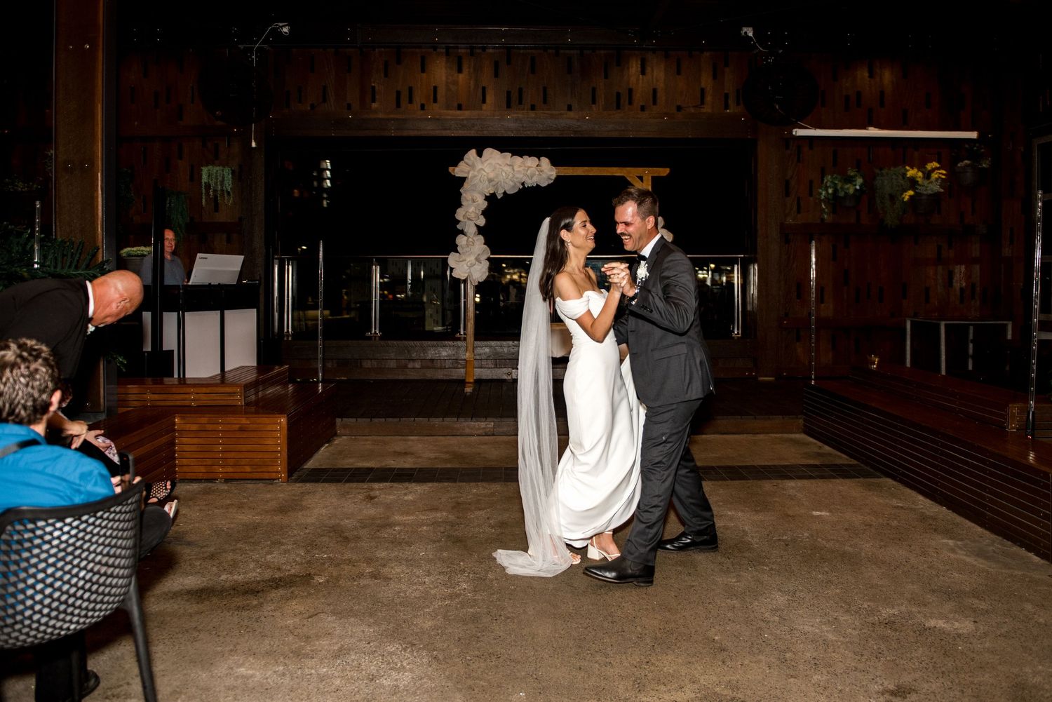 Bride and groom share their first dance at an elegant indoor wedding reception with a floral arch backdrop.