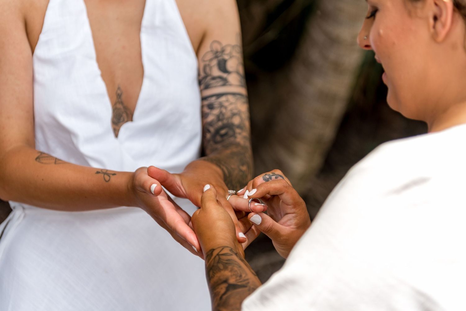 Close-up of two women exchanging wedding rings during intimate beach ceremony.