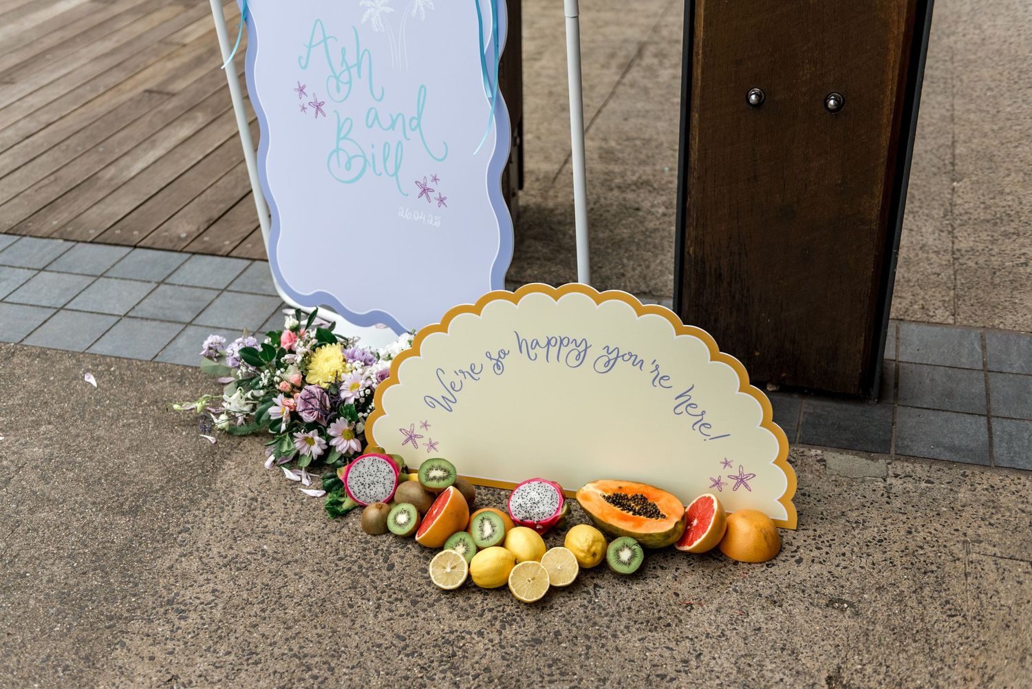 Colorful tropical wedding welcome sign for Ash and Bill decorated with fresh fruit and flowers.